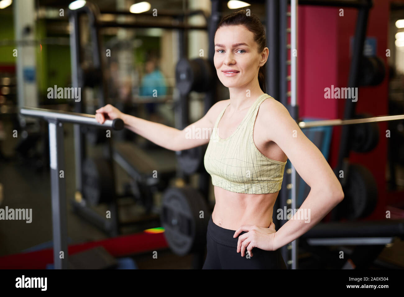 Waist up portrait of fit young woman smiling looking at camera while posing against machines in modern gym, copy space Stock Photo