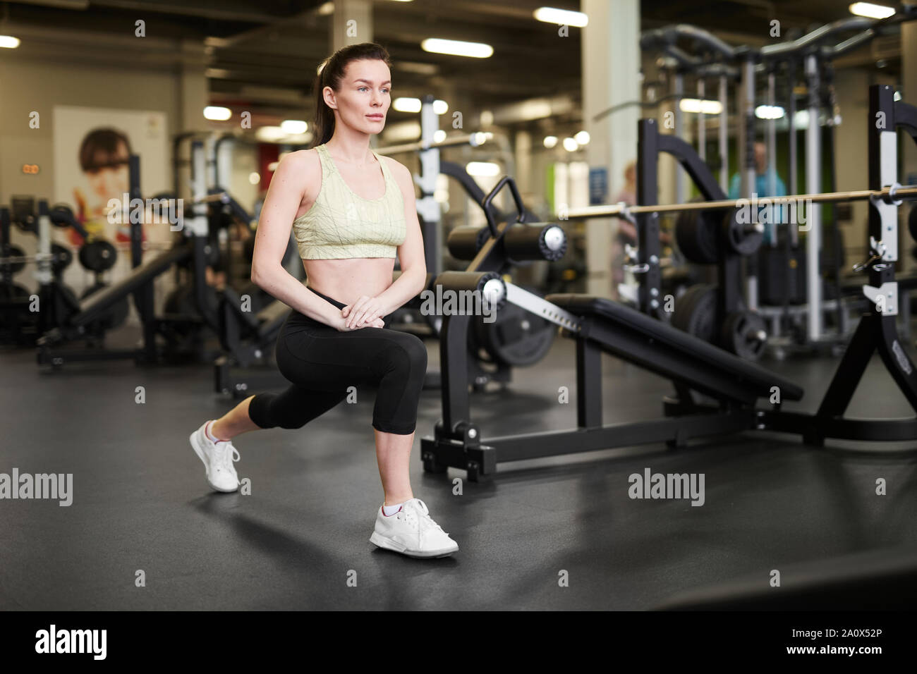 Full length portrait of fit young woman stretching legs during workout in modern gym, copy space Stock Photo