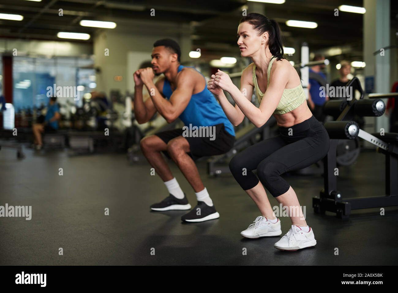 Side view portrait of sportive couple doing squats during fitness workout in modern gym, copy space Stock Photo