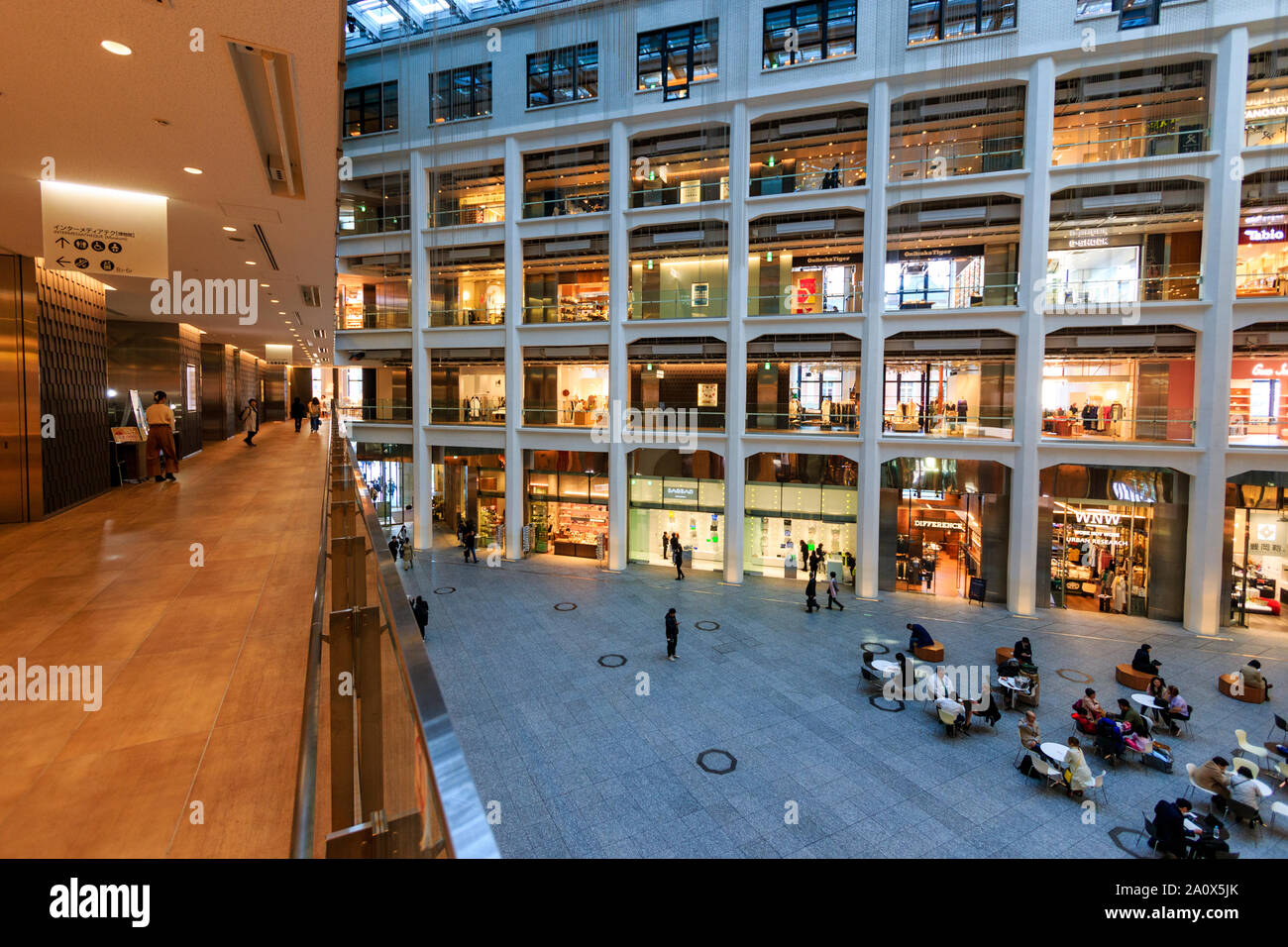 Tokyo, Marunouchi. JP tower KITTE building interior. The triangular atrium, aisle, shops and ground floor seating area with people sitting. Daytime. Stock Photo
