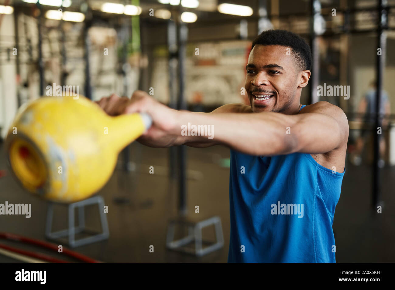 Waist up portrait of strong African-American man swinging kettlebell during cross workout in modern gym, copy space Stock Photo