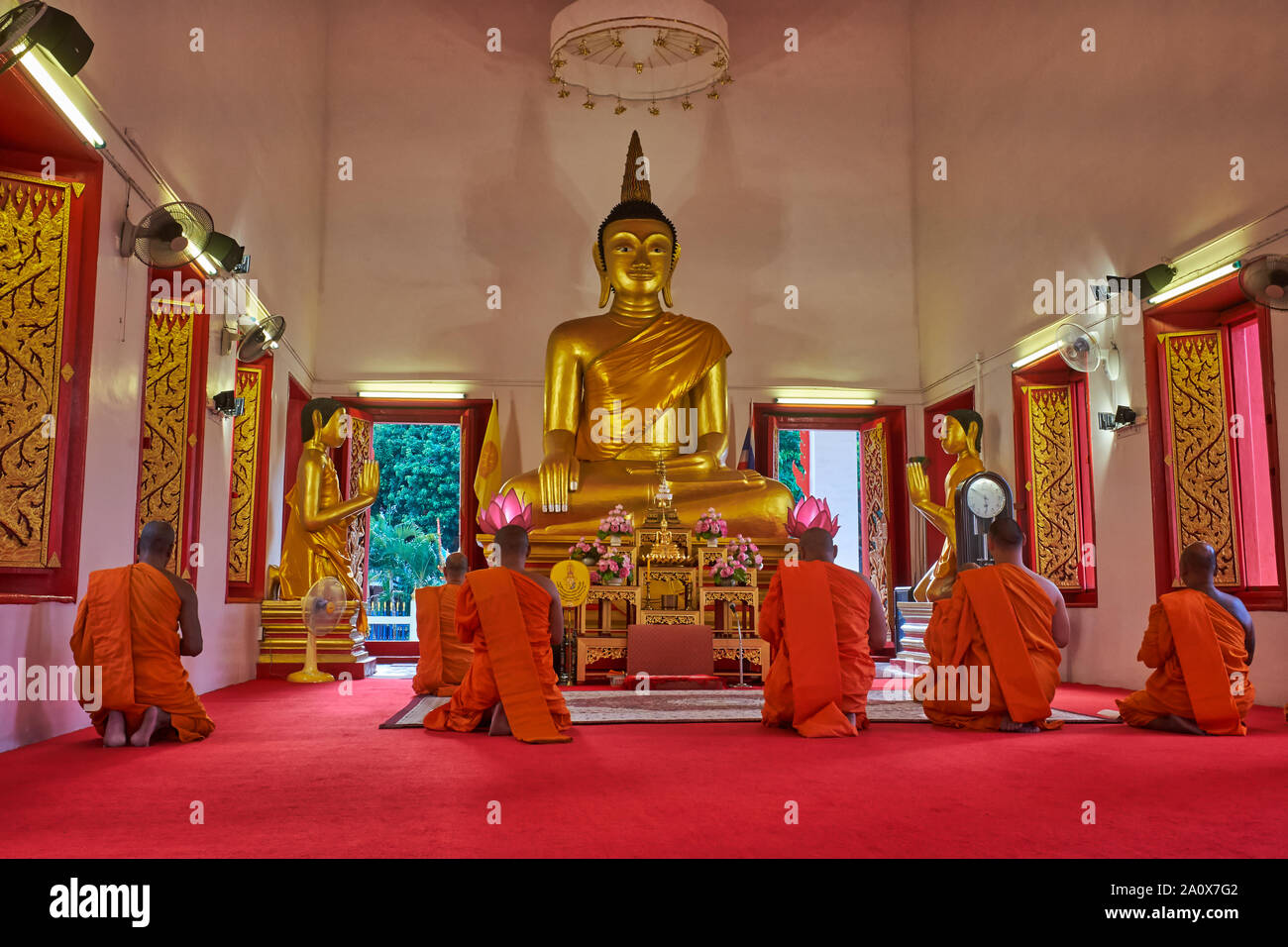 Monks in Wat Mongkon Nimit (Mongkolnimit) in Phuket Town, Thailand, sit in front of the temple's Buddha statue for their evening prayer and meditation Stock Photo
