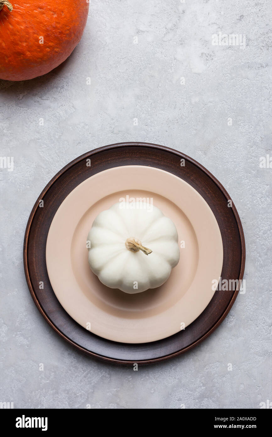 Seasonal empty plate with pumpkin on gray concrete background with orange squash in corner. Concept of thanksgiving table set Stock Photo