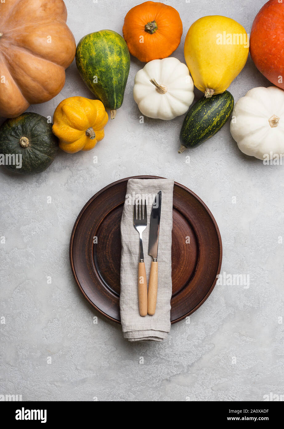 Table set with pumpkins, empty plate, napkin, knife and fork. Card for harvest banner. Concept of crop serving plate on concrete gray background Stock Photo