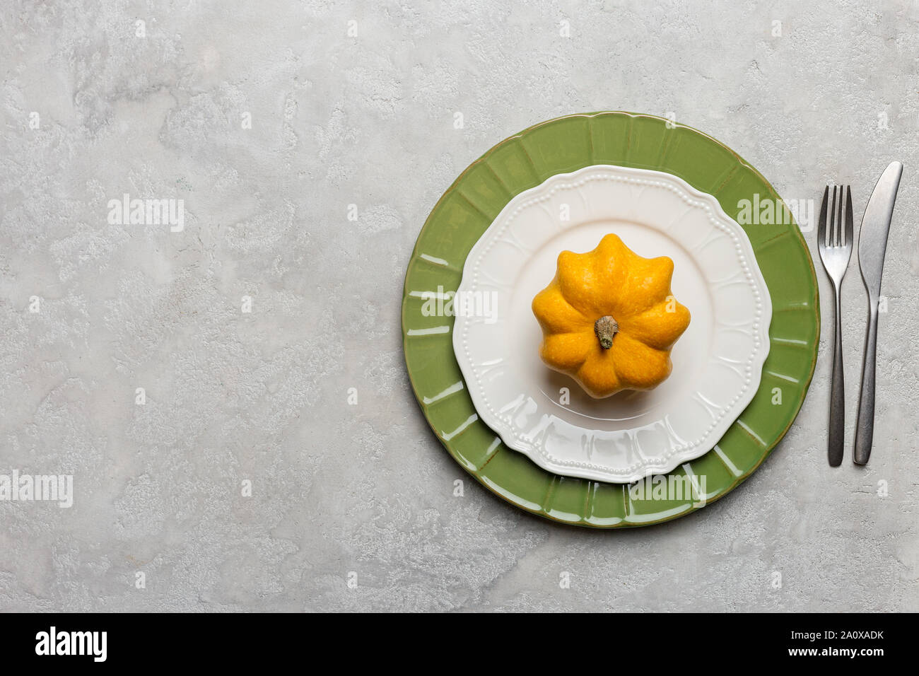 Table set with whole decor yellow pumpkin on empty plate. Horizontal image for text. Concept of harvest and Thanksgiving table set. Minimal top view, Stock Photo