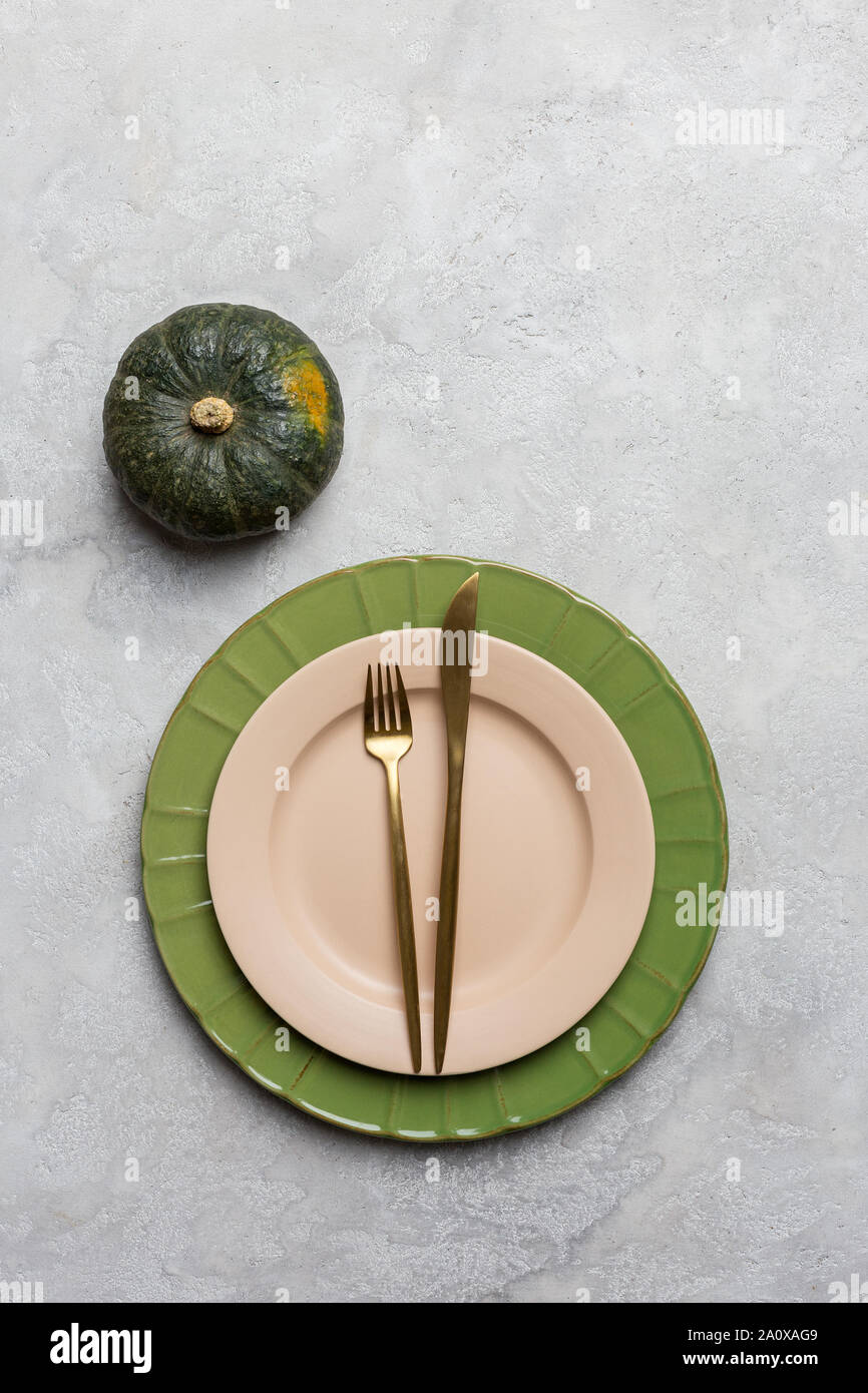 Empty plate with golden tableware on gray background with green pumpkin near. Concept of Halloween's and Thanksgiving's dinner table set. Above view, Stock Photo