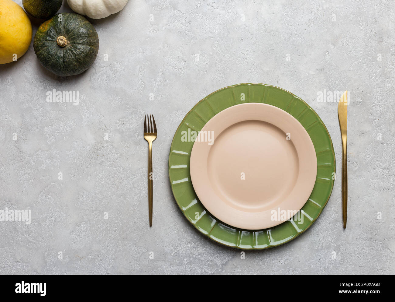 Seasonal table setting on gray concrete background with pumpkins and golden fork and knife. Stock Photo