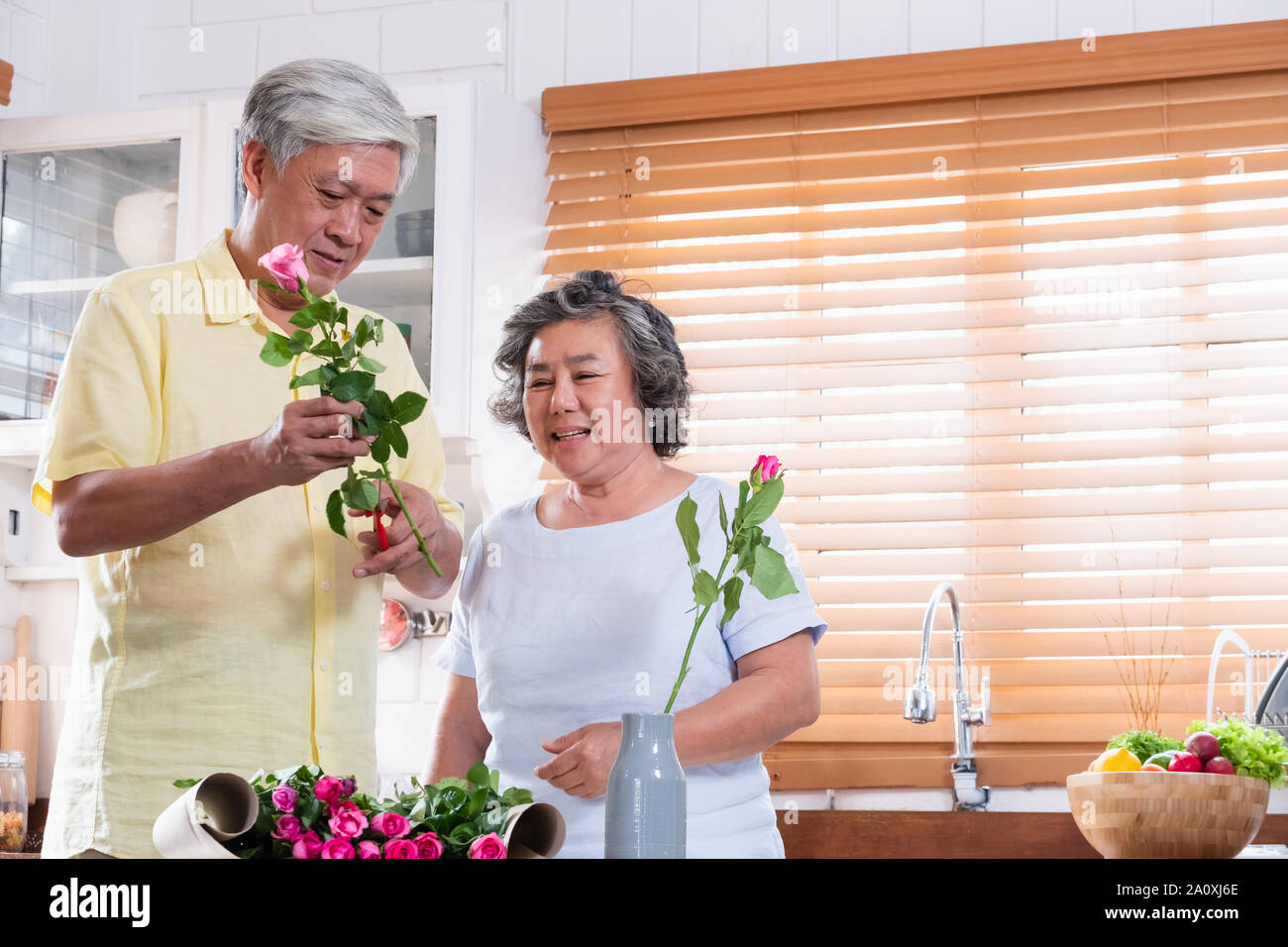Asian Senior couple husband and wife flower arrangement to vase on table in kitchen at home in Valentine's Day.lovely senior couple concept Stock Photo