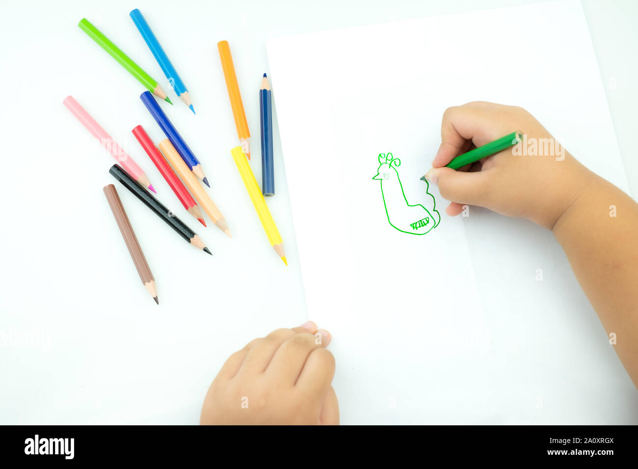 Children draw paints in the playroom, A child is holding a crayon in his hands at paper and crayons for drawing on the table, Hand Kids drawings,  chi Stock Photo