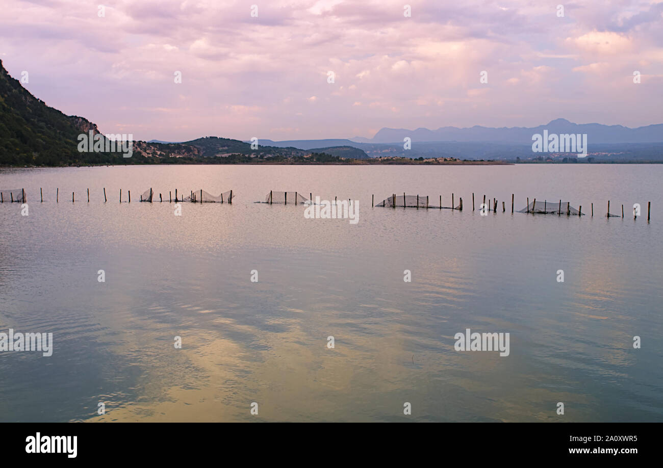 Sky mirroring on water surface and posts with metal mesh fence in Gialova sea lagoon, Peloponesse, Greece at sunset time. Stock Photo