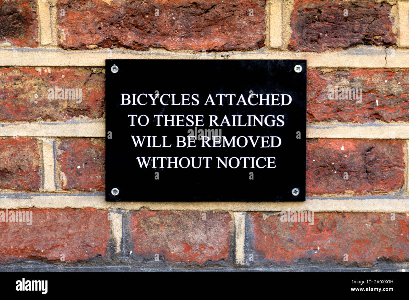 'Bicycles attached to these railings will be removed without notice' sign on a brick wall Stock Photo