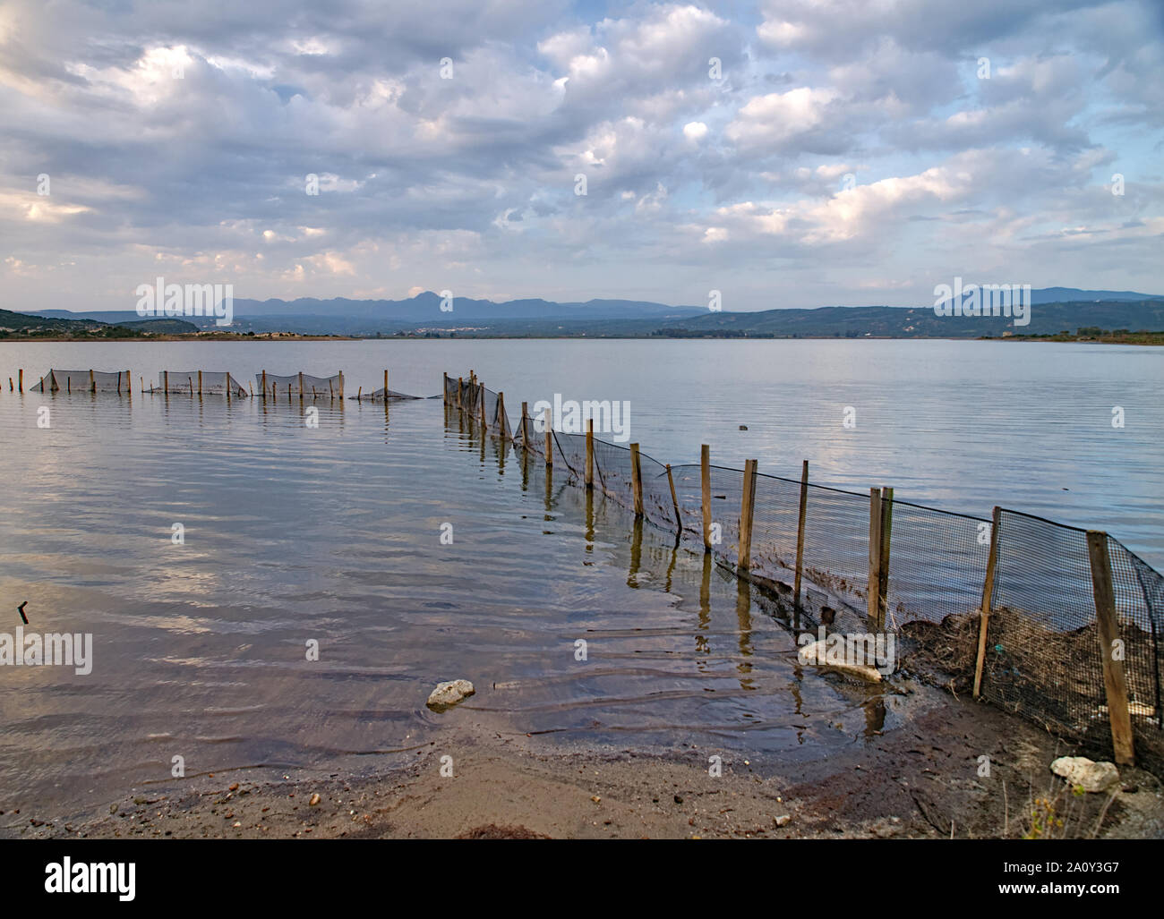 Wooden posts with metal mesh fence in Gialova sea lagoon, Peloponesse, Greece. Dramatic cloudy sky over sea rippled water surface. Stock Photo
