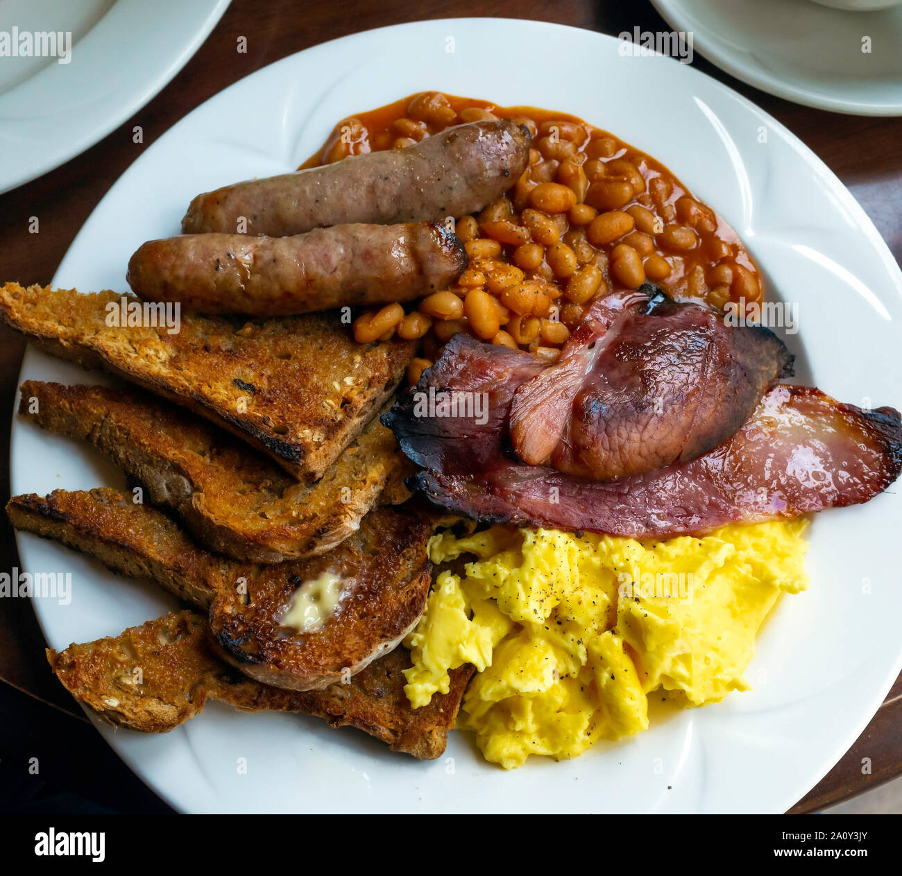 English farmhouse  Breakfast with well-done bacon scrambled egg sausages baked beans with brown granary buttered toast Stock Photo
