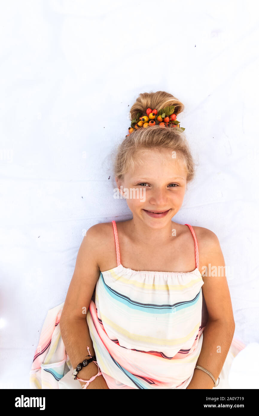 Close up portrait of adorable little girl lying on white background with stylized long blond hair with red brier adornment Stock Photo