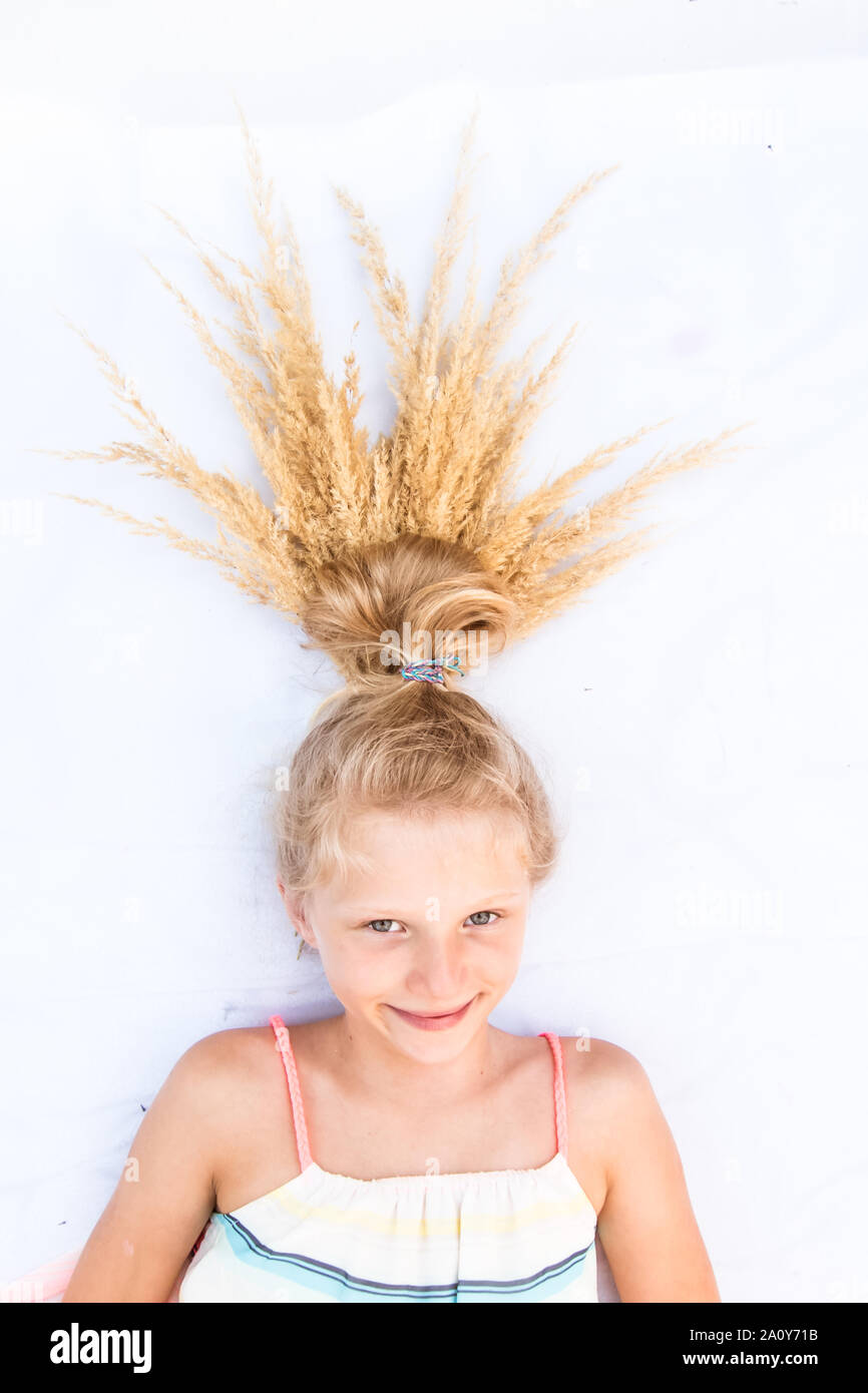 Close up portrait of adorable little girl lying on white background with stylized long blond hair with adornment Stock Photo
