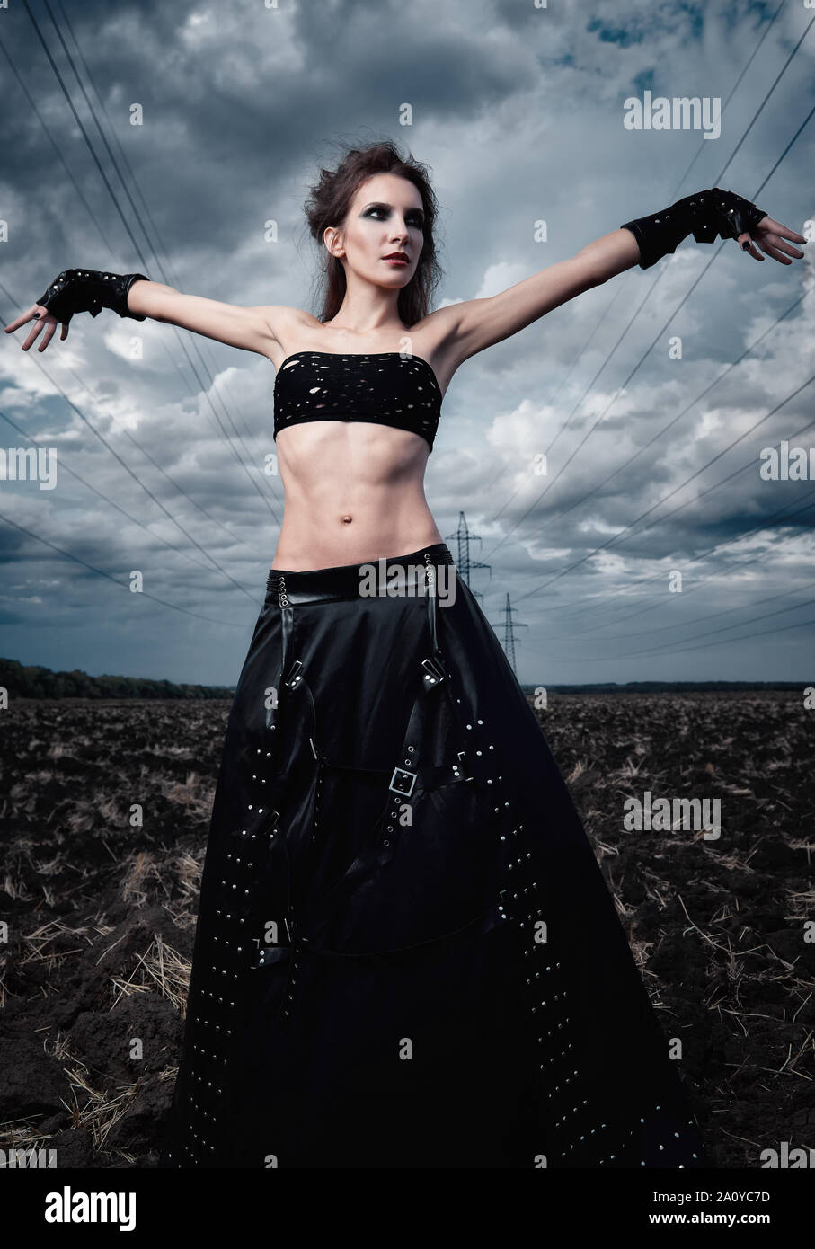 Informal fashion: the beautiful slender young gothic girl dressed in black  leather skirt and gloves. Outdoor portrait in field near pylons and power l  Stock Photo - Alamy