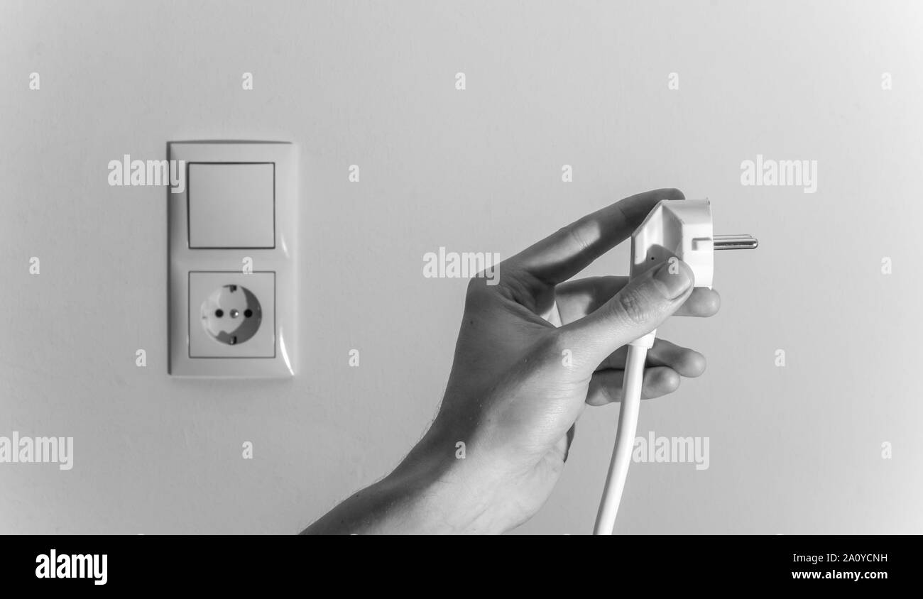 White plug with cable in males hand, ready to connect. Energy concept ...