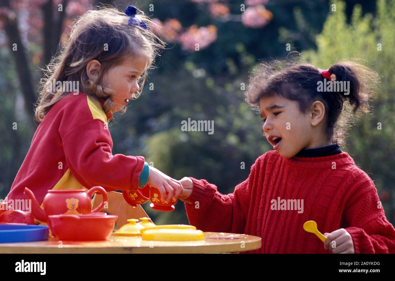 two little girls playing outdoors fighting over toy tea set Stock Photo