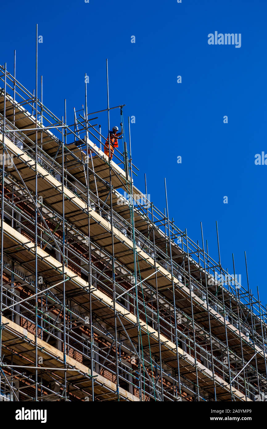 Construction worker standing on top of scaffolding, pulling up materials to the top of the building Stock Photo