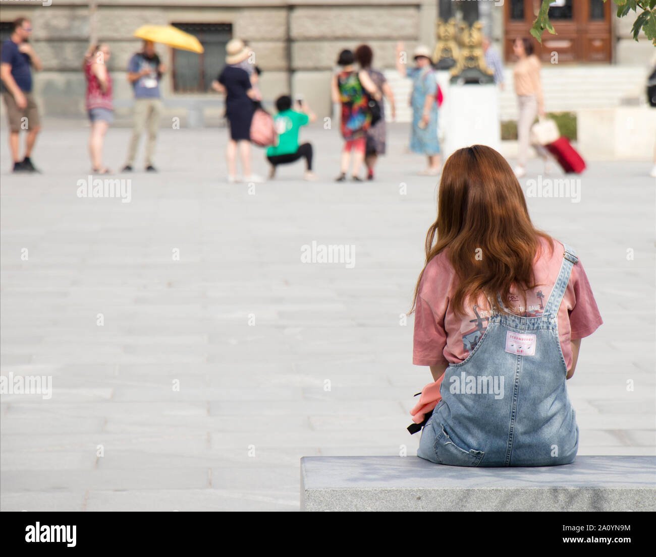 Belgrade, Serbia - September 12, 2019 : One young teenage girl with ginger hair in jeans overall sitting and waiting on city bench on town square, and Stock Photo