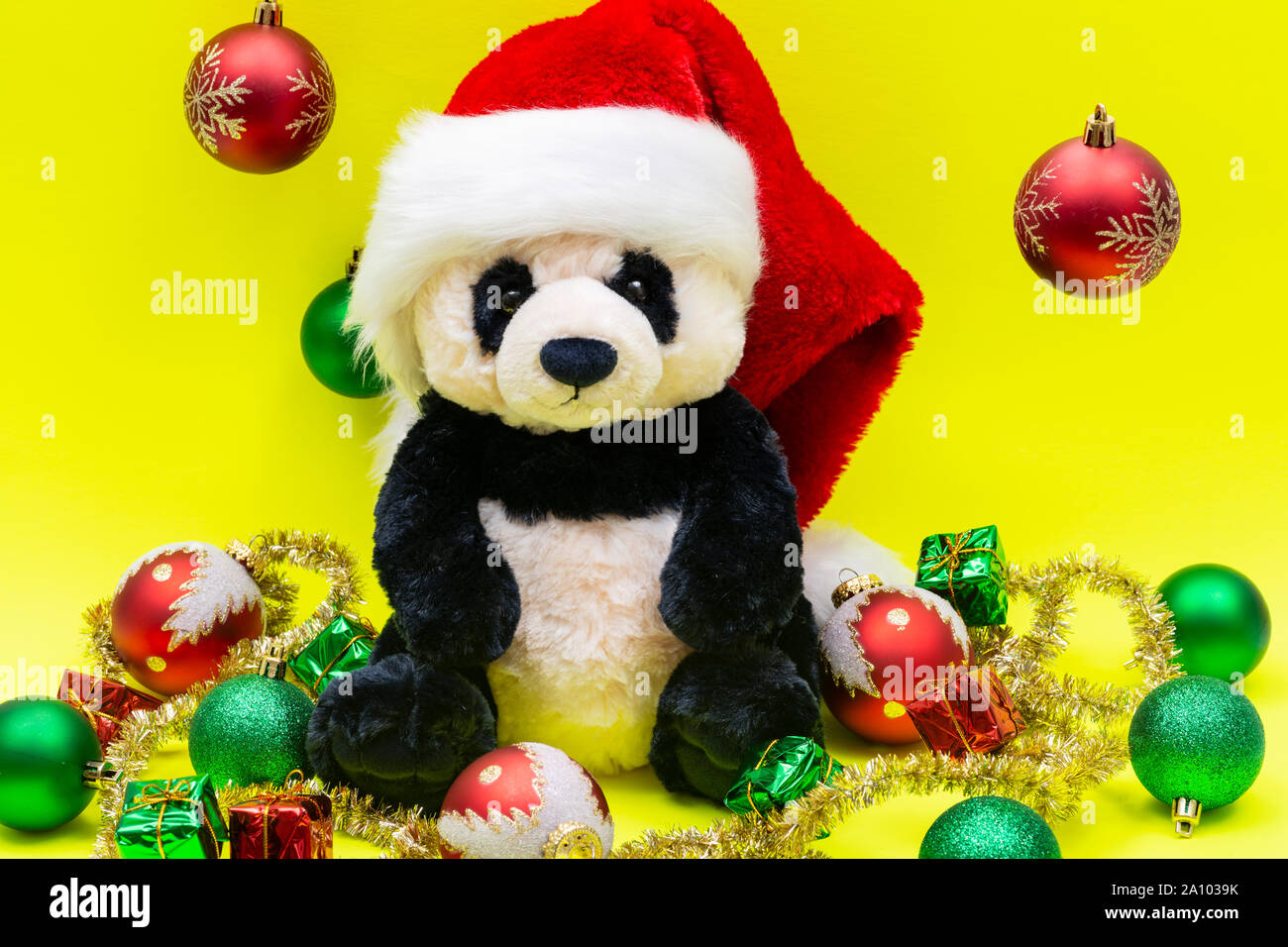 Panda Bear plush toy with Red Christmas Santa Hat surrounded by Tinsel Garland and Vintage Ornaments on bright yellow background. Holidays concept. Stock Photo