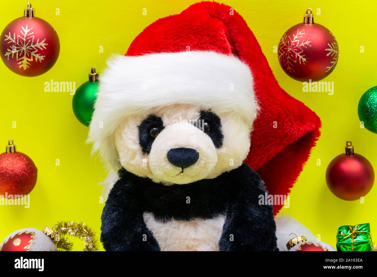 Panda Bear plush toy with Red Christmas Santa Hat surrounded by Tinsel Garland and Vintage Ornaments on bright yellow background. Holidays concept. Stock Photo