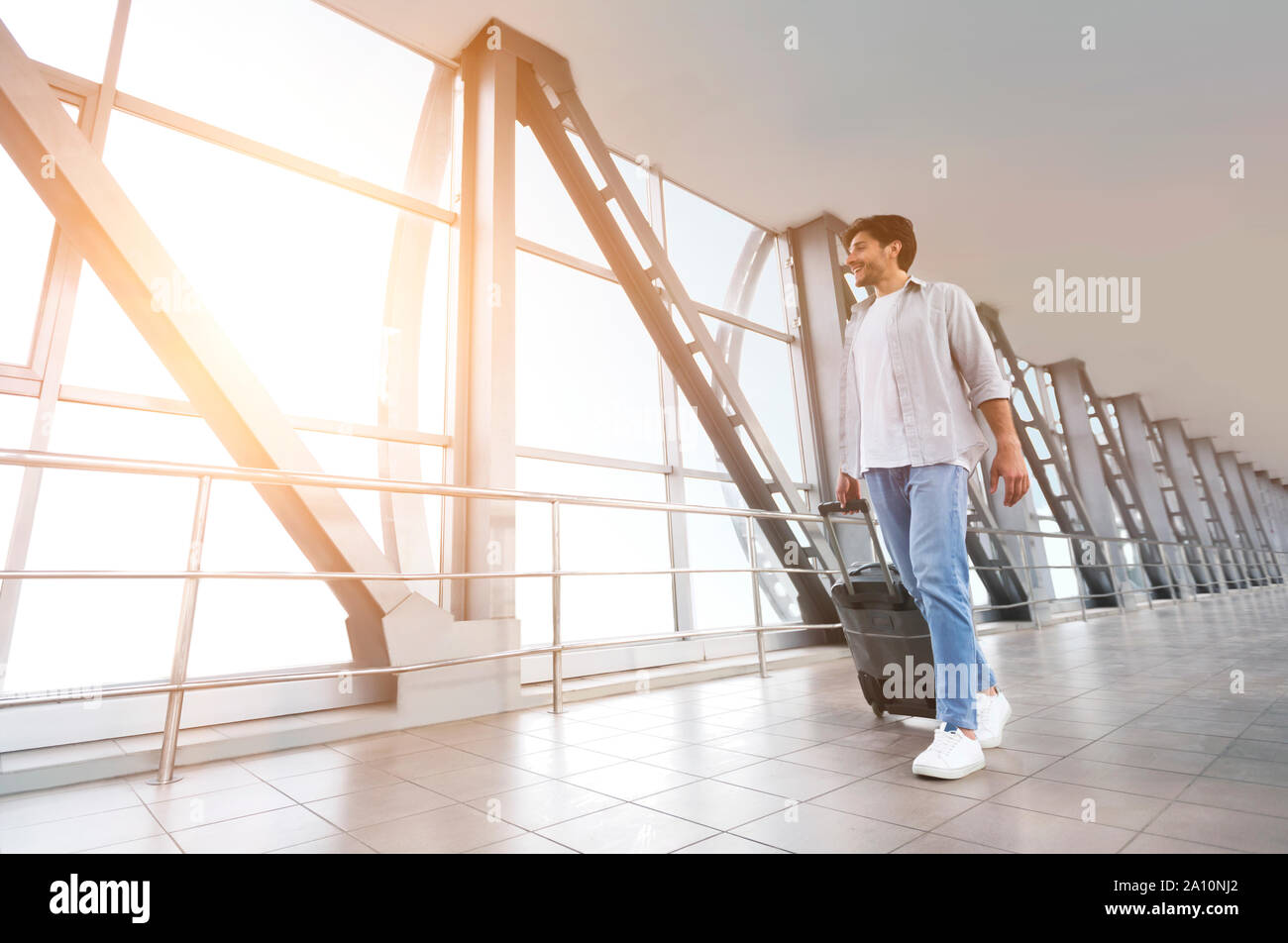 Cheerful man walking with luggage in airport terminal Stock Photo - Alamy