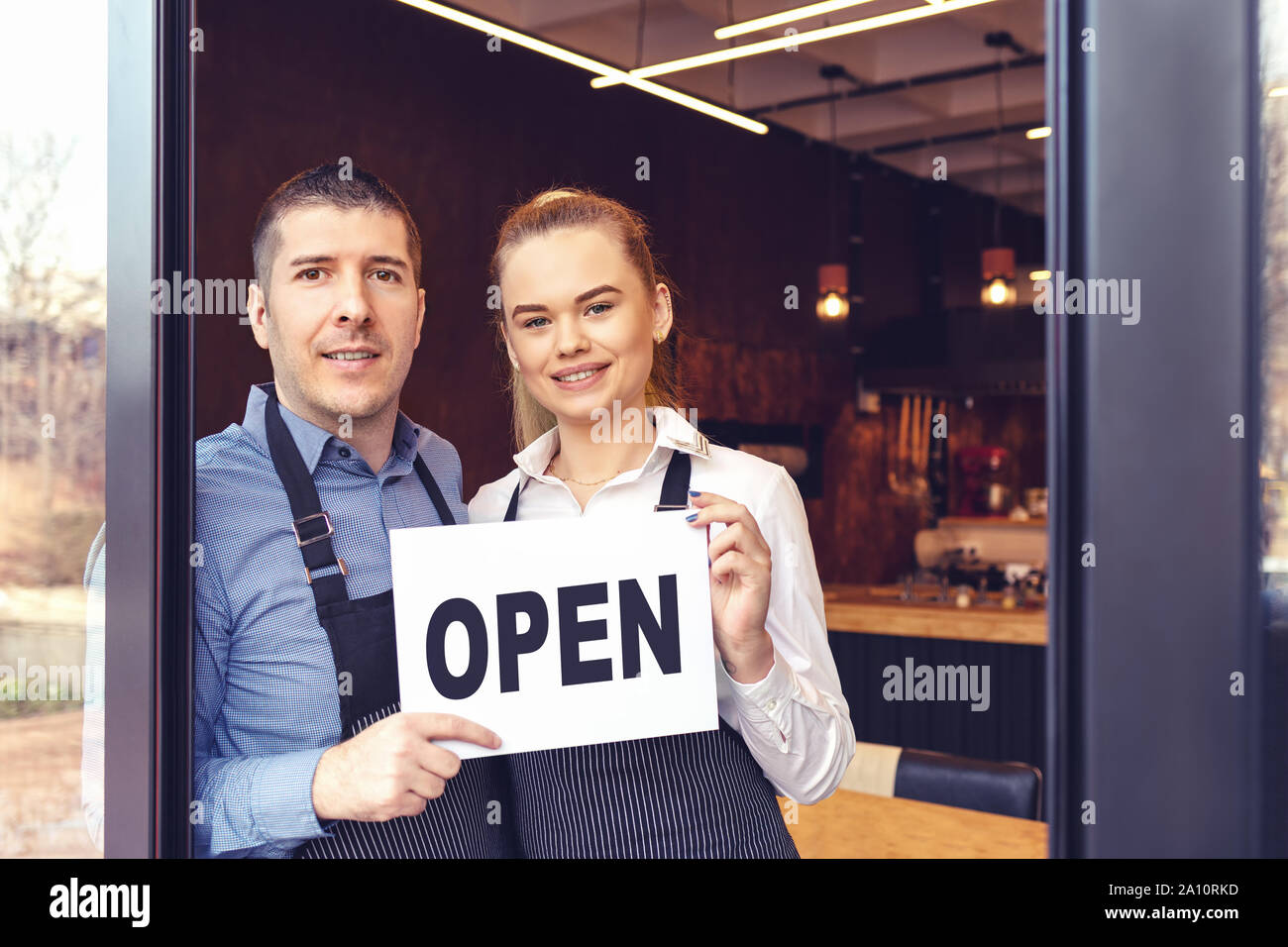 Two cheerful small business owners smiling and looking at camera while standing at entrance door Stock Photo
