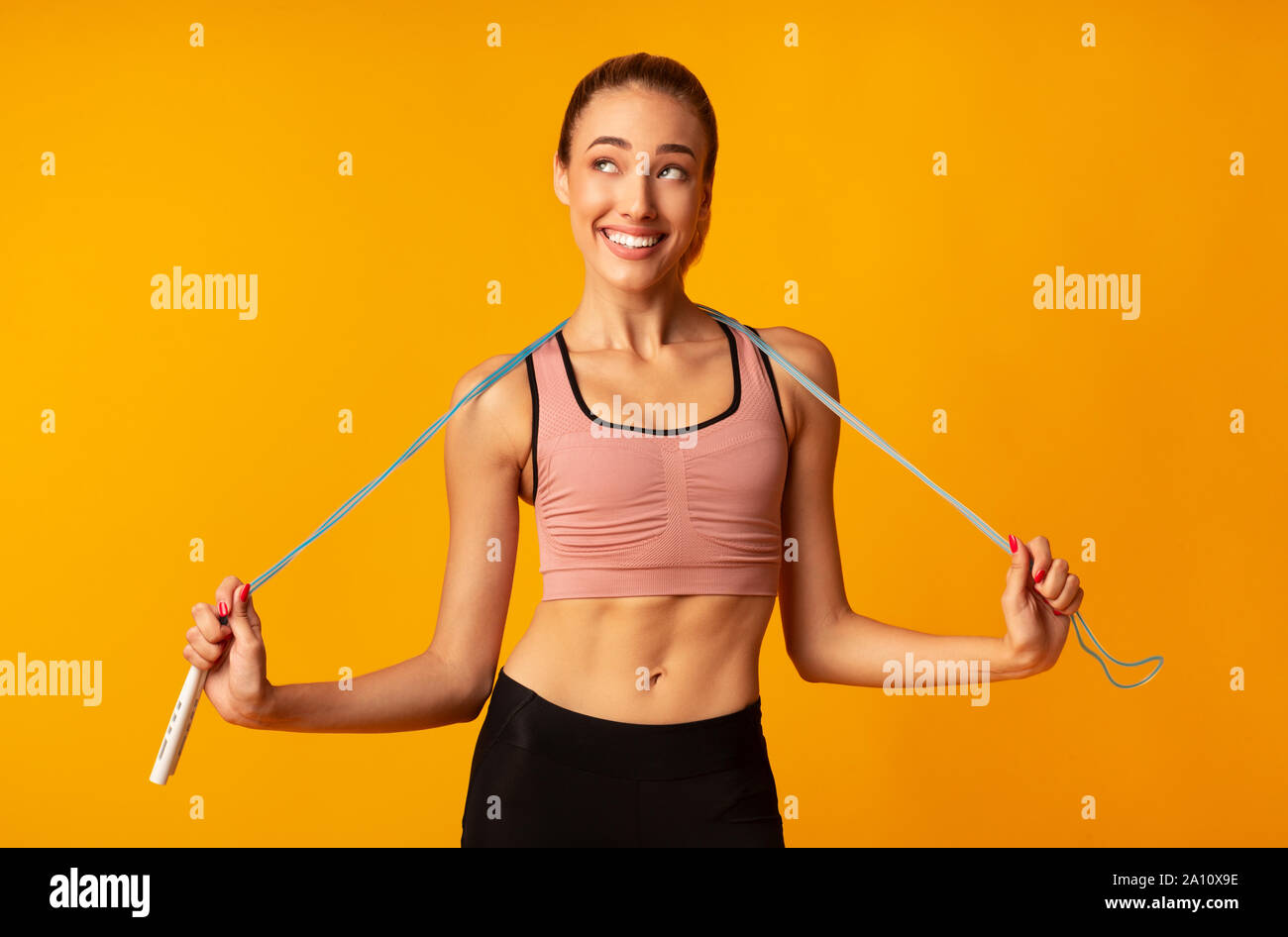 Slim Girl Holding Jump Rope Over Yellow Background Stock Photo