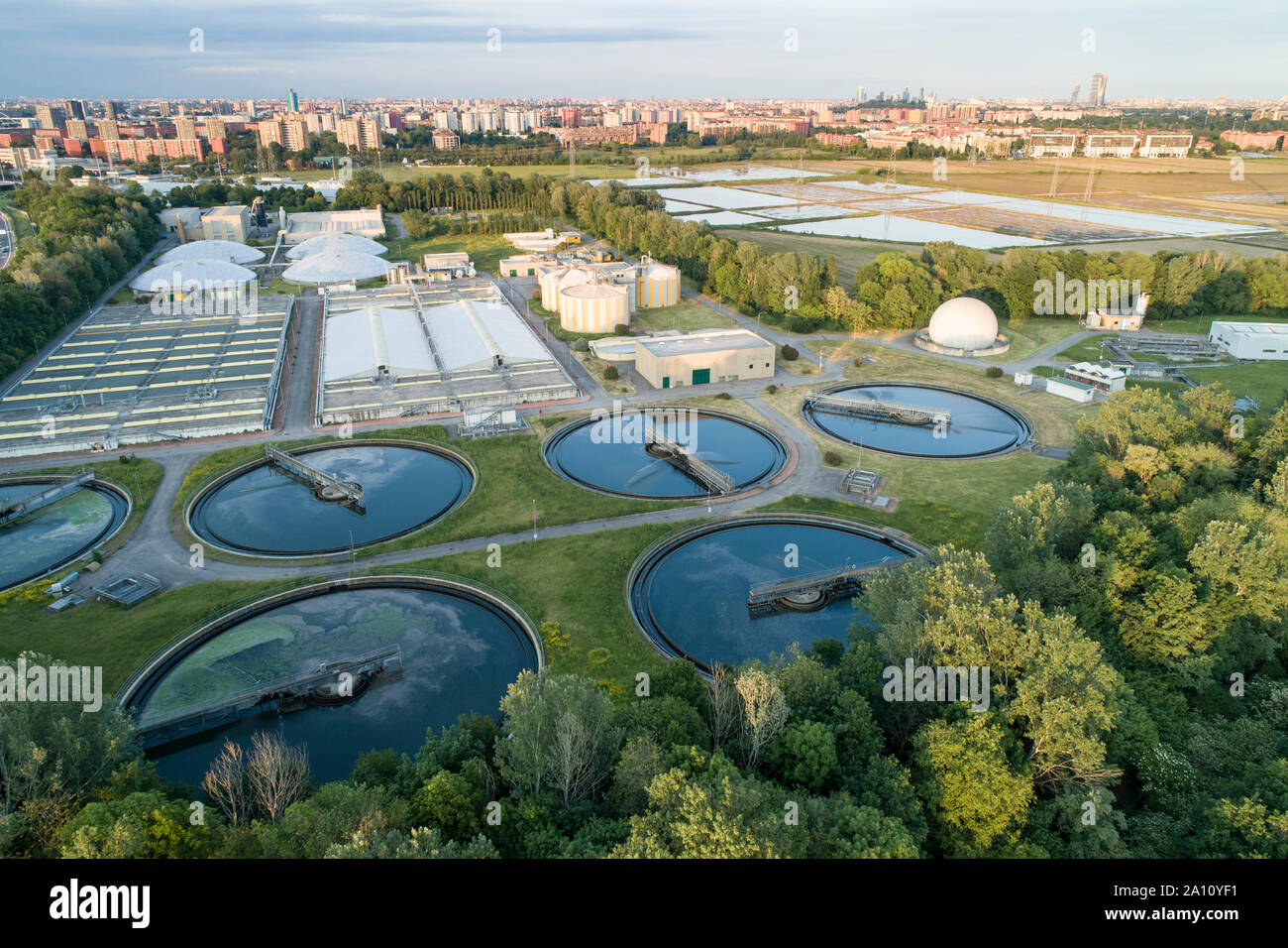 Flying over sewage treatment plant. Aerial view of industrial water treatment for the city in background. Waste water purification. Stock Photo