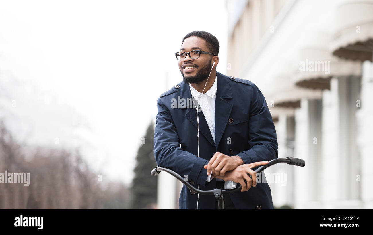 Afro businessman riding on bike to work and listening music Stock Photo