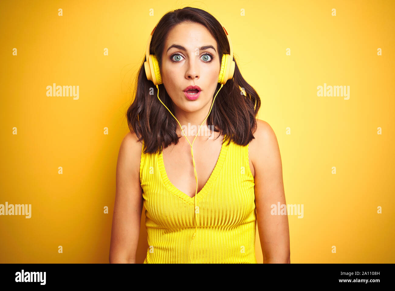 Young beautiful woman listening to music using headphones over yellow ...