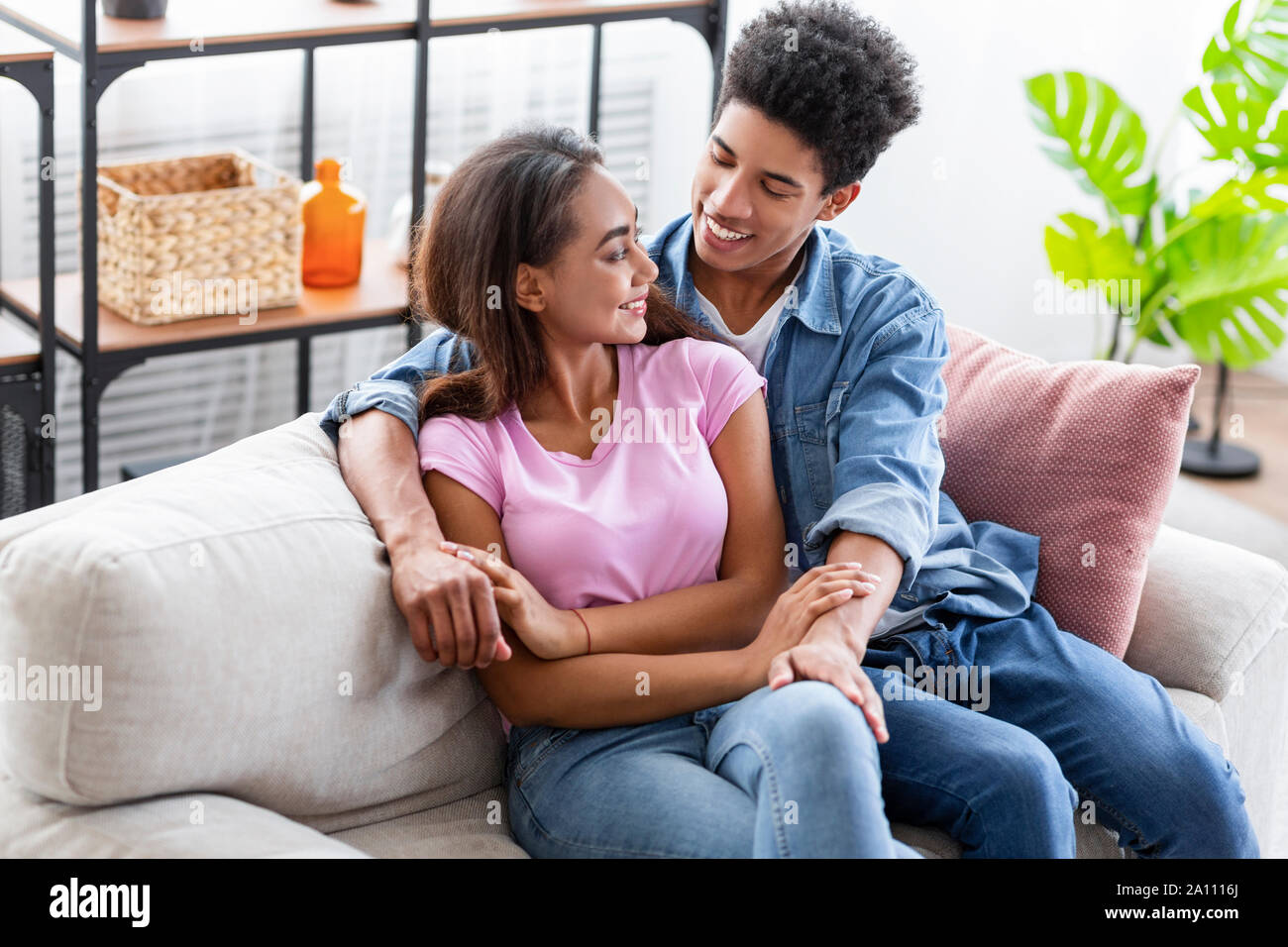 Smiling teenagers cuddling and glancing to each other at home Stock Photo