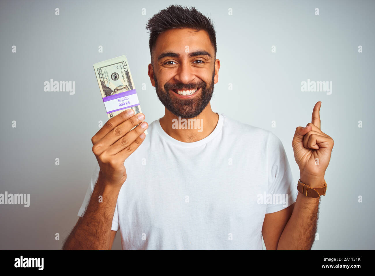Young indian man holding dollars standing over isolated white ...