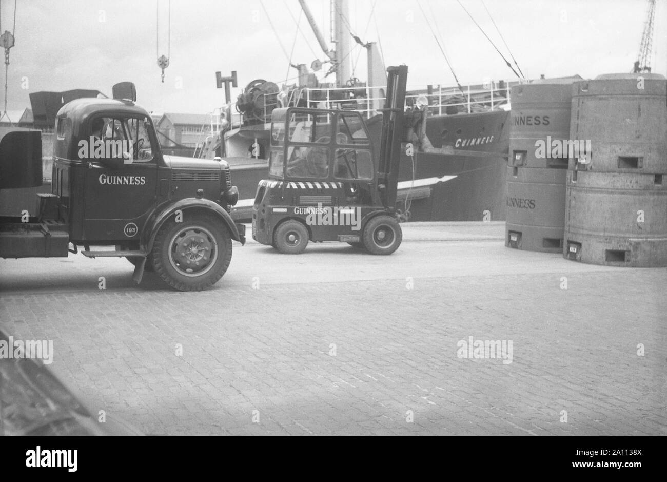 Shipping Guinness beer in giant metal beer kegs (transportable tanks) by truck to the docks to be loaded on to ships by fork-lift trucks, Dublin, Eire c. 1955 Stock Photo