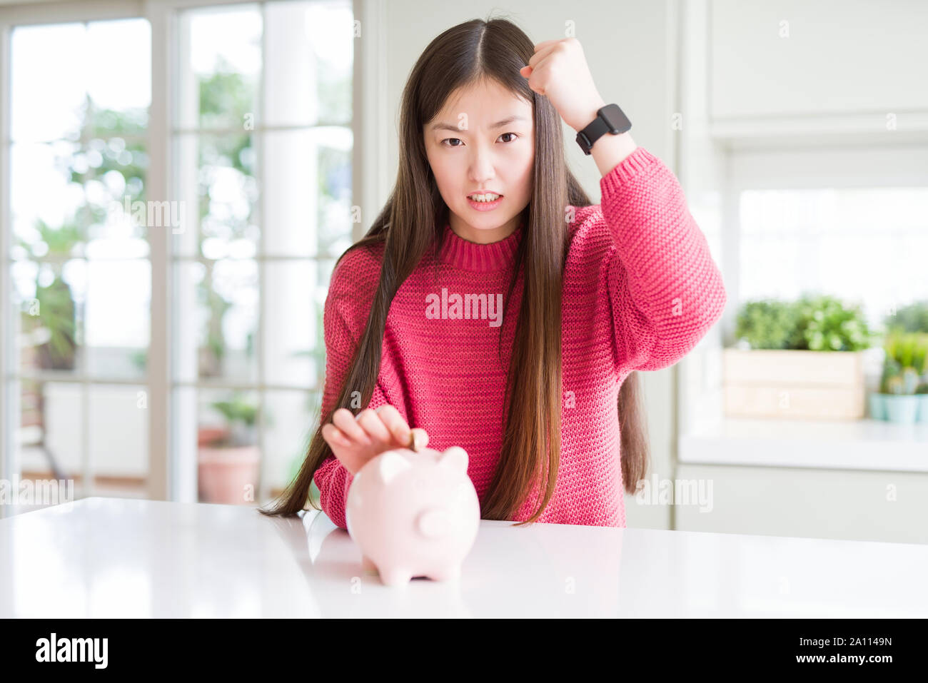 Beautiful Asian woman putting a coin inside piggy bag annoyed and ...