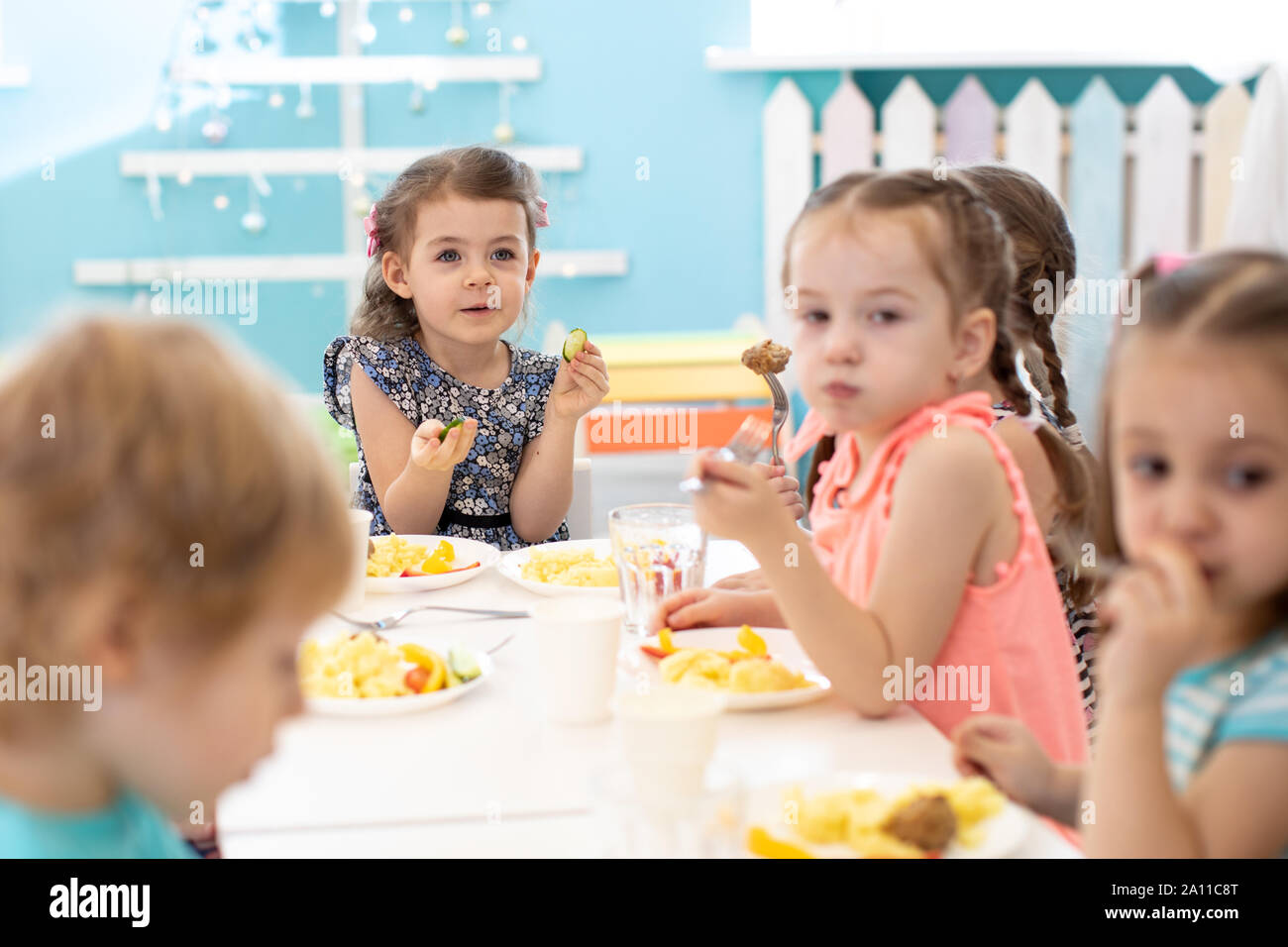 Group of children sitting at the table with lunch and eat appetizing. Kids have a dinner in