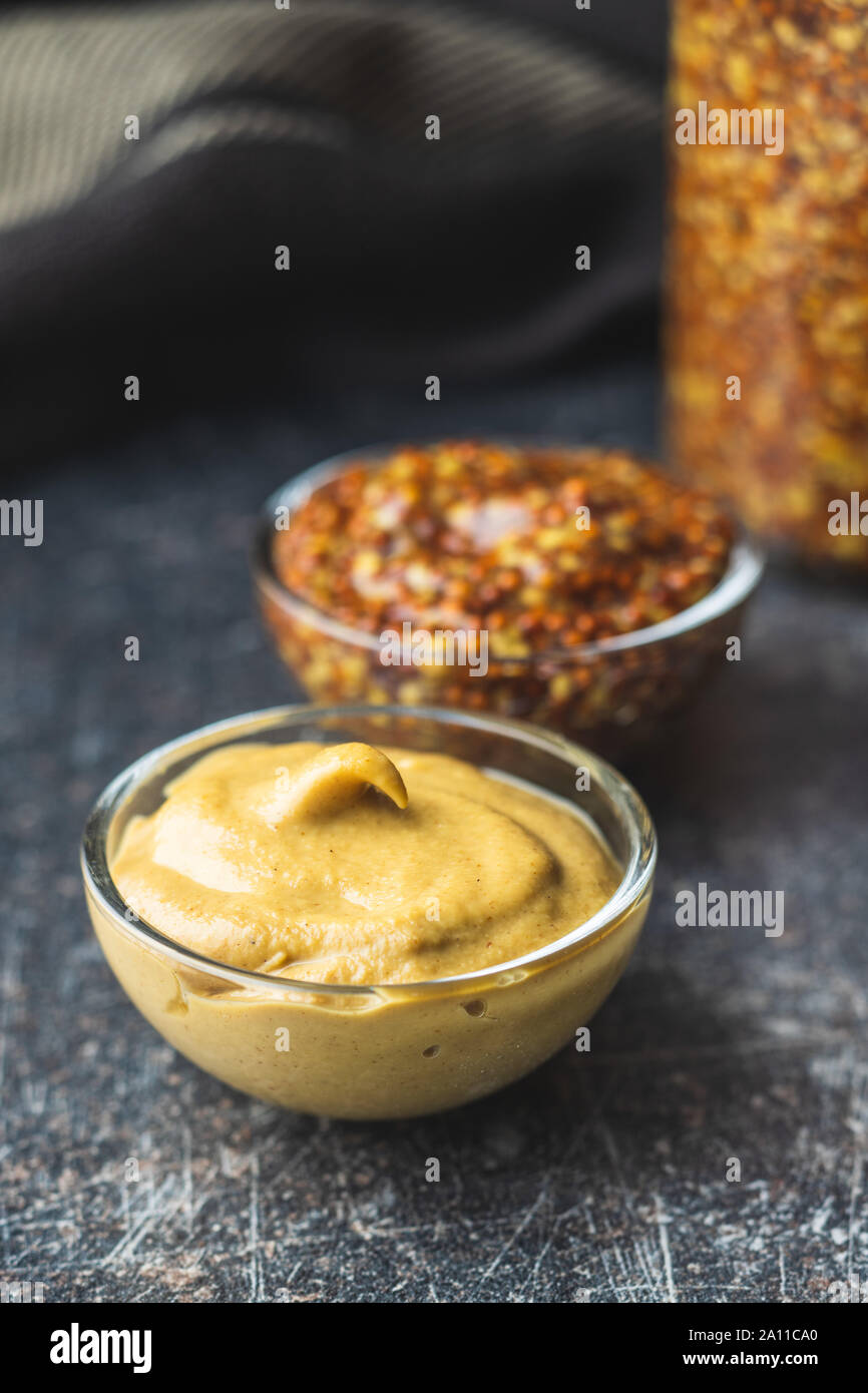 Yellow mustard and whole grain mustard in bowl on old kitchen table. Stock Photo