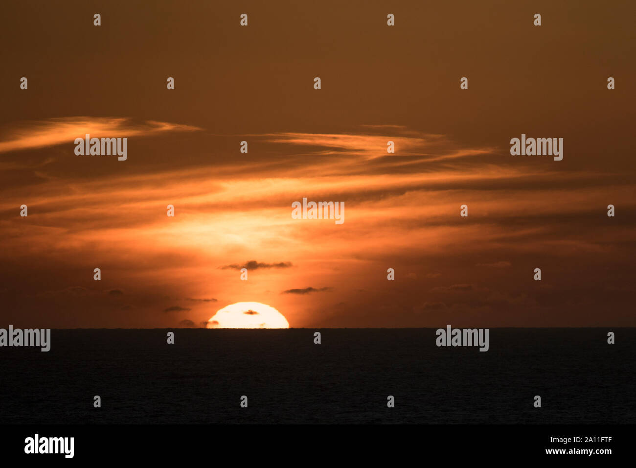 A sun half setting into the Pacific Ocean Stock Photo