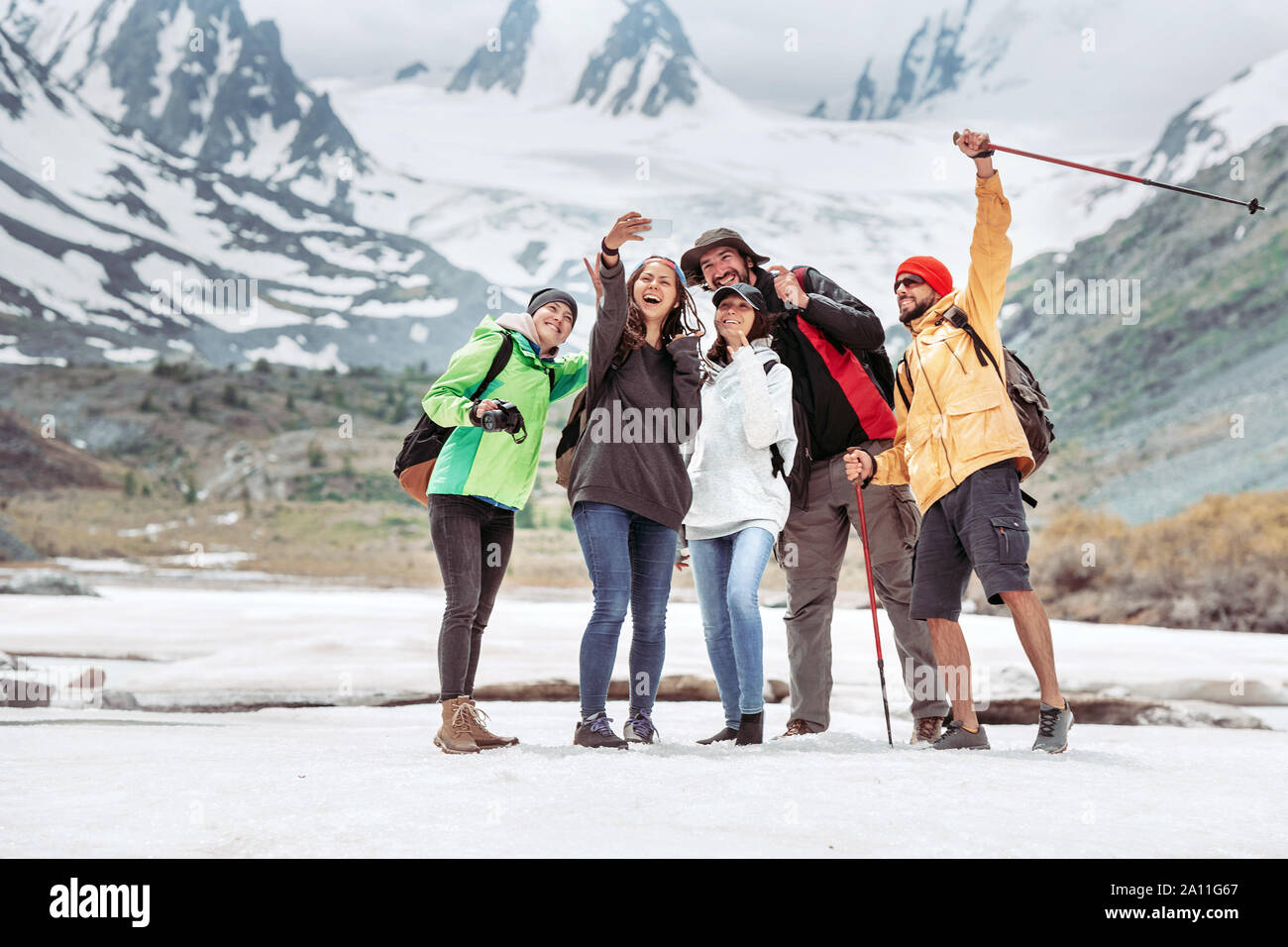 Group of five happy tourists is taking selfie photo against mountains Stock Photo