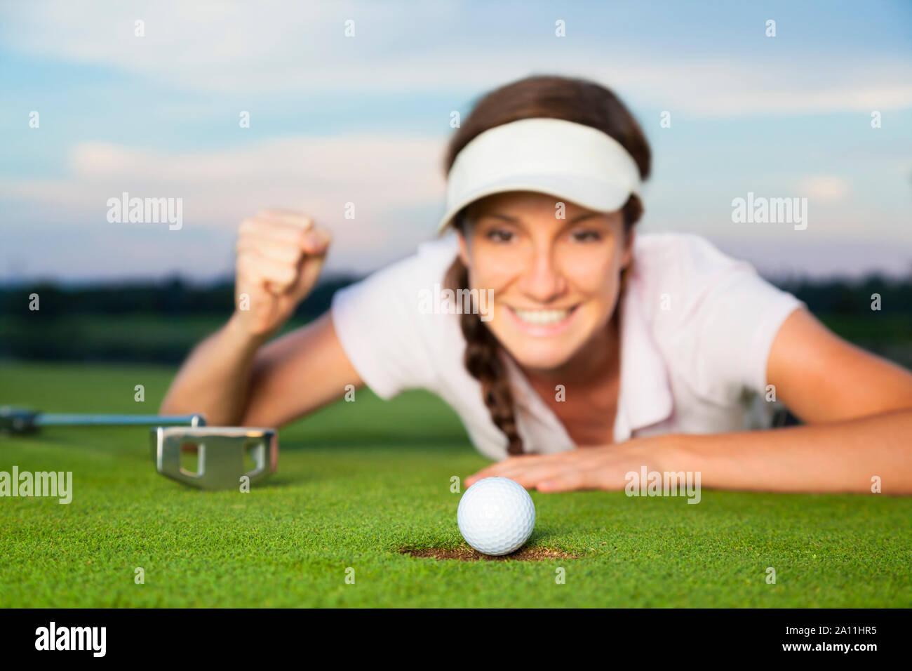 Joyous girl golfer looking at ball dropping into cup. Stock Photo