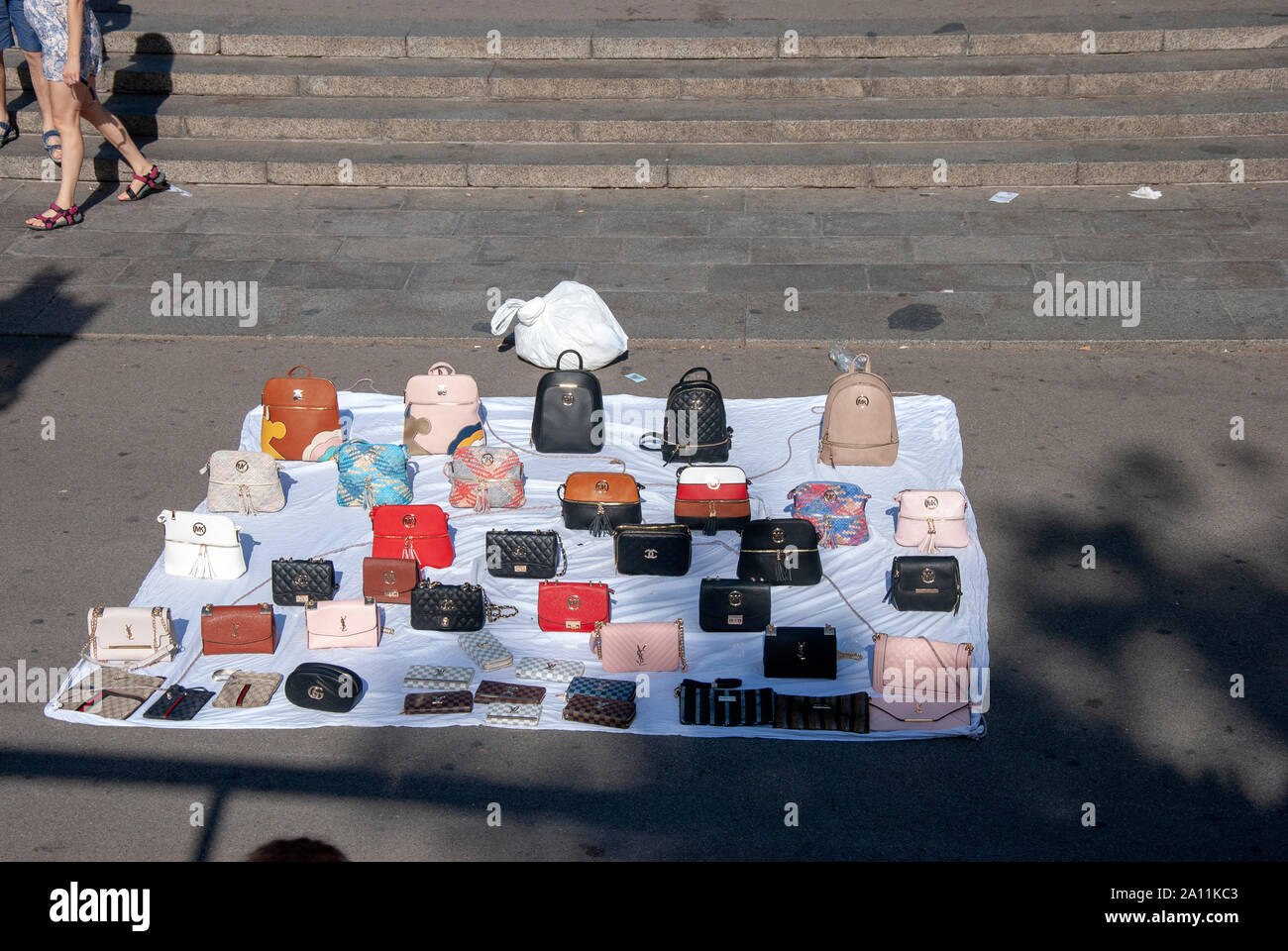 Illegal Street Traders Display of Fake Designer Goods on White Sheet Placa de Catalunya Barcelona Catalonia Spain pavement offering Gucci Michael Kors Stock Photo