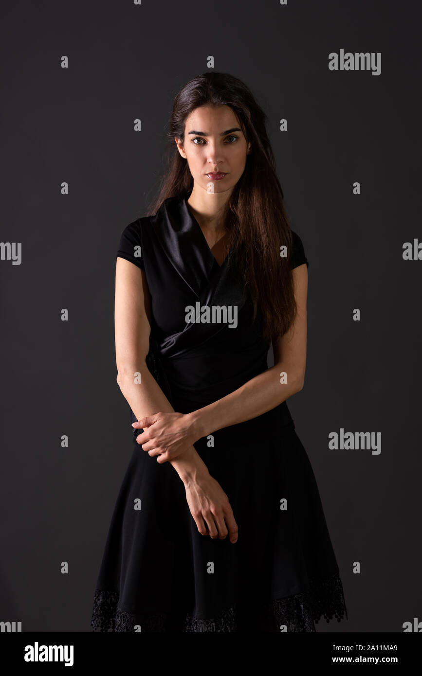 A beautiful serious young woman in an elegant black dress standing in ...