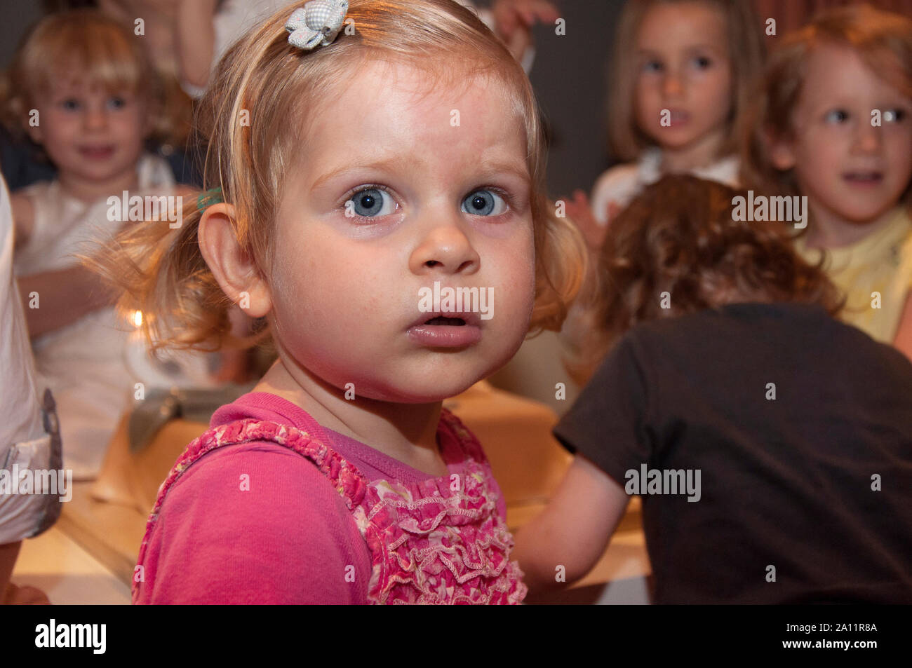 Candid authentic close up portrait of an adorable cute three years of age old blonde hair little girl with blue eyes at a kid's party. Stock Photo