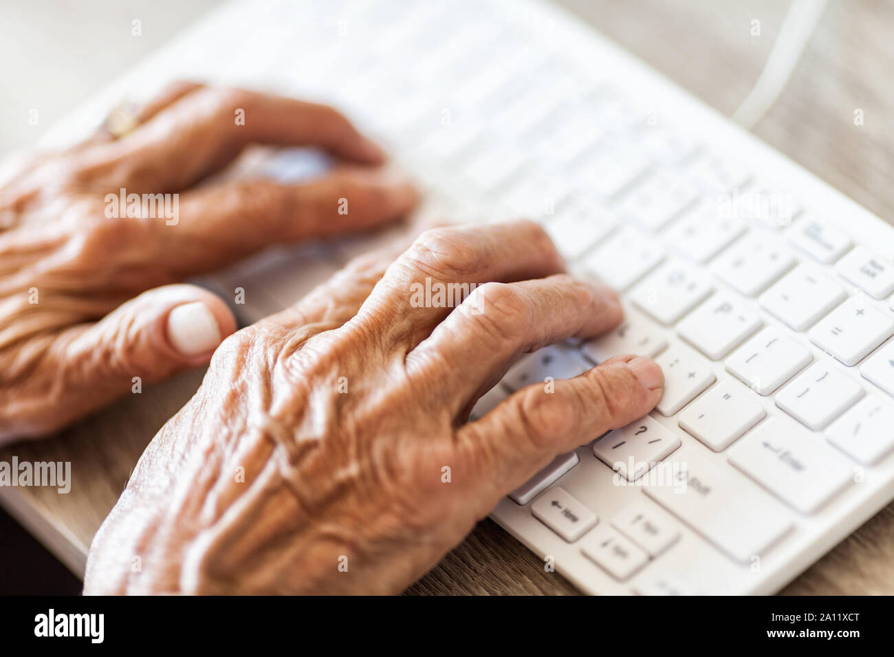 Elderly woman typing on a PC keyboard Stock Photo