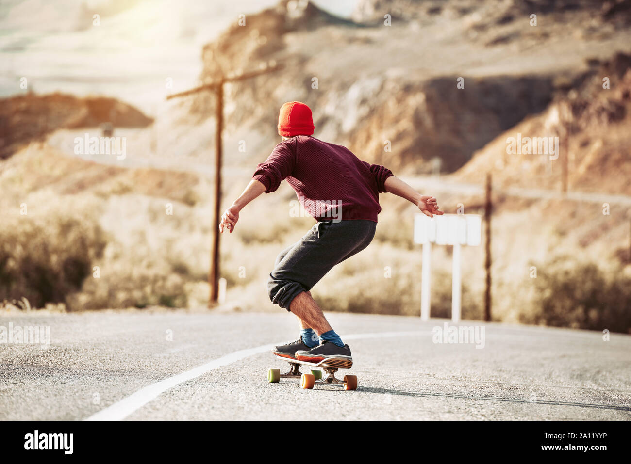 Hipster rides by mountain road on longboard or skateboard Stock Photo