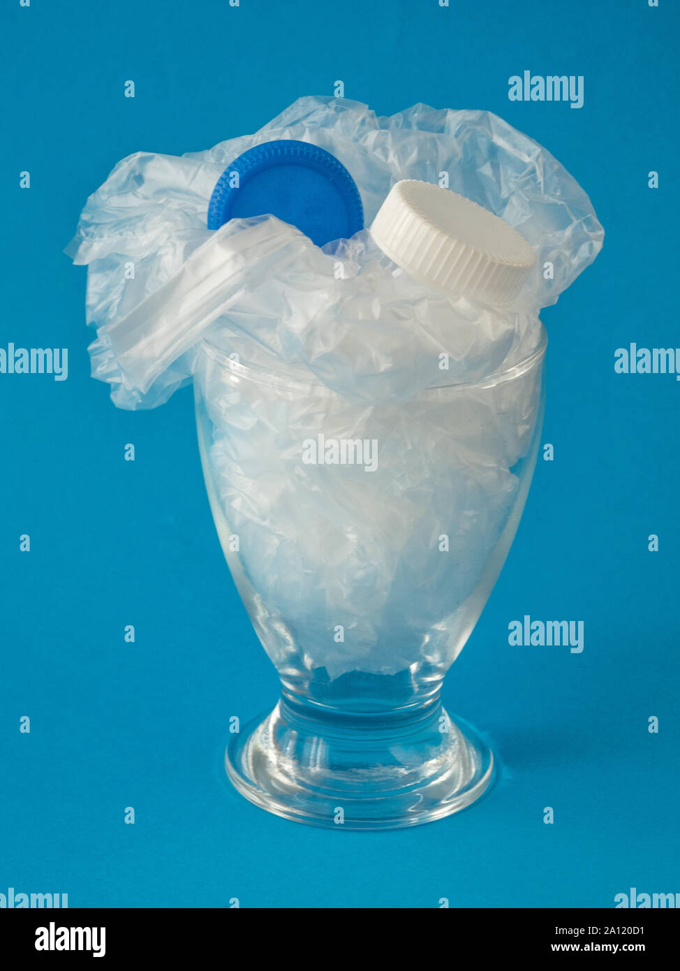 Glass with plastic inside on blue background - drinking plastic environmental concept Stock Photo