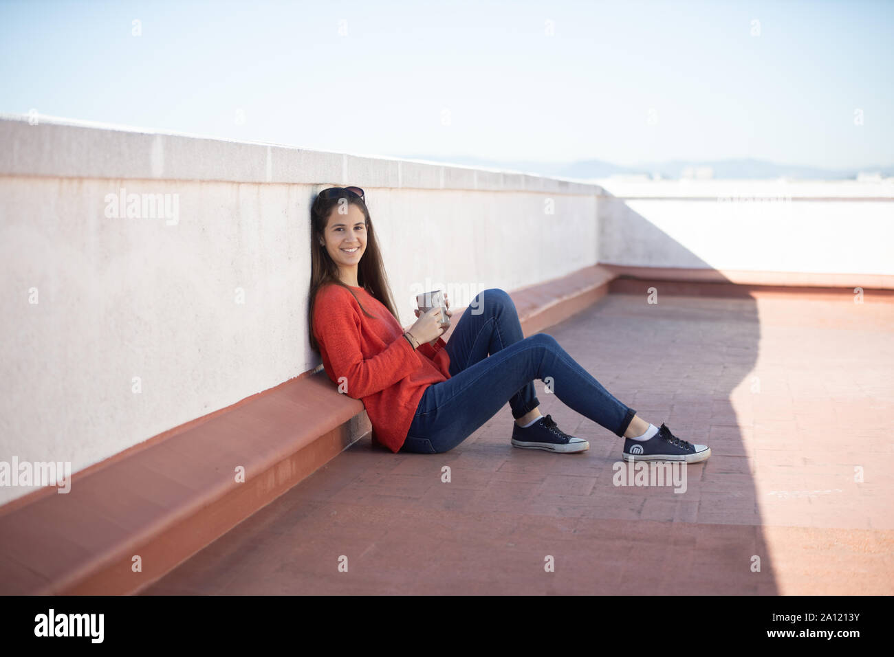 Chica adolescente feliz tomando un café sentada en la azotea Stock Photo
