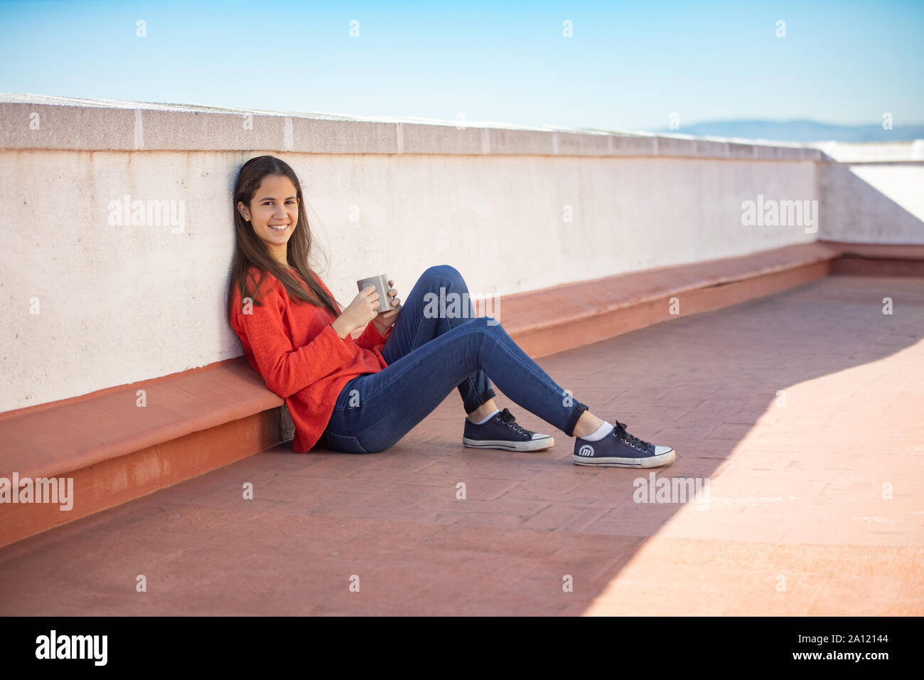 Chica adolescente feliz tomando un café sentada en la azotea Stock Photo