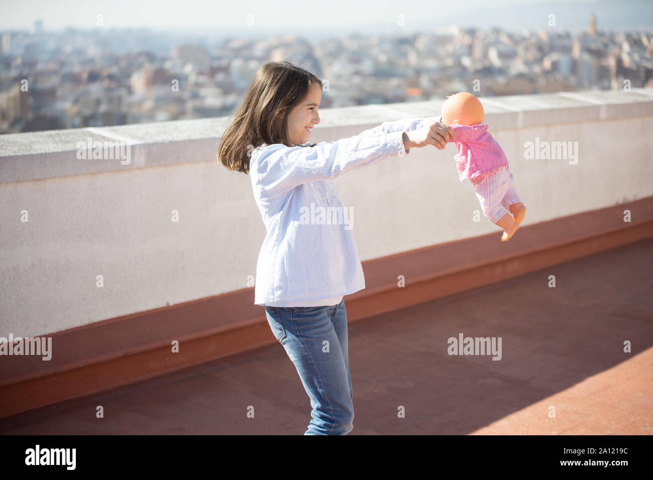 Niña de pie jugando con una muñeca en la azotea Stock Photo